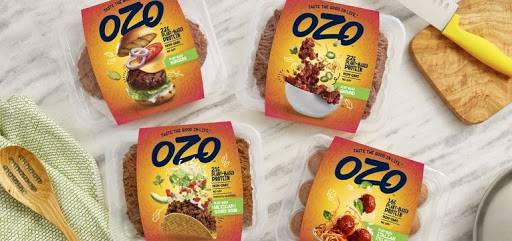 Promotional image showing various Ozo-brand plant-based meat products arranged on a rustic kitchen table.