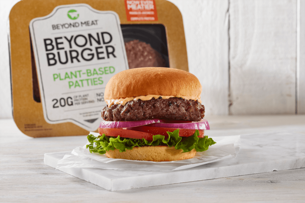 Promotional image of a Beyond Meat-brand burger on a white roll with product packaging visible in the background.