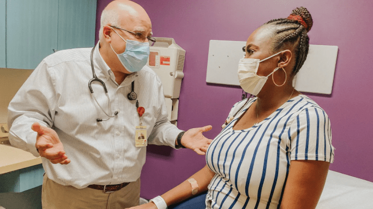 A male doctor and a female patient talking in an office while wearing masks